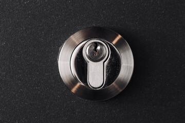 Modern metal lock detail. Close up of round security cylinder on black surface. Safety system...