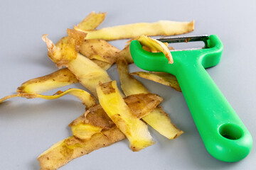 Green peeler with pile of potato peels on a gray surface