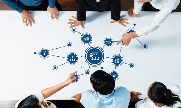 A group of professionals engages in collaborative strategy development around a table featuring a visual data flow. Interaction and teamwork enhance productivity and creativity. Amity