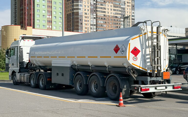 Trucks with trailers of fuel tanks are parked next to a huge oil storage barrel. Truck with white...