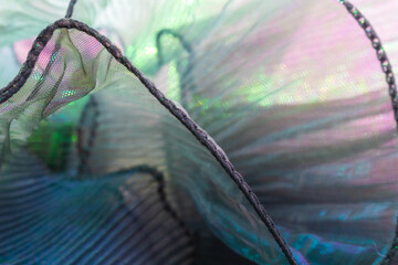 Close-up of iridescent fabric with shimmering green and purple hues, featuring delicate folds and...