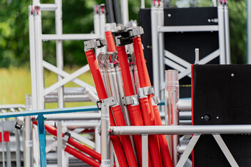 Stack of aluminum scaffolding parts and red safety-wrapped support poles at construction or event site, modular framework equipment for building, stage, or maintenance setup