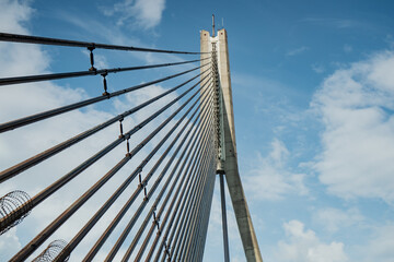 Suspension bridge cables and tower structure reaching into blue sky, modern architectural detail of steel tension wires, engineering construction concept for transport and infrastructure