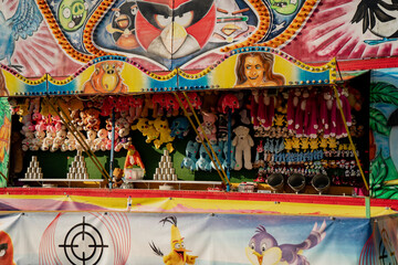 Colorful carnival shooting gallery game booth with plush toy prizes and painted decorations at outdoor fairground on sunny summer day creating festive playful atmosphere