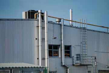 Industrial building exterior with metal walls, pipes, chimneys and access ladder under clear sky...