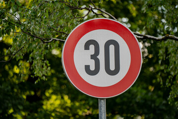 Traffic sign with 30 speed limit on urban street surrounded by green trees indicating road safety rules and vehicle speed restriction for drivers in residential neighborhood © K