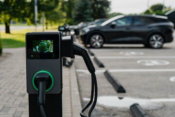 Electric vehicle charging point in parking lot with black cars plugged in to charger highlighting...