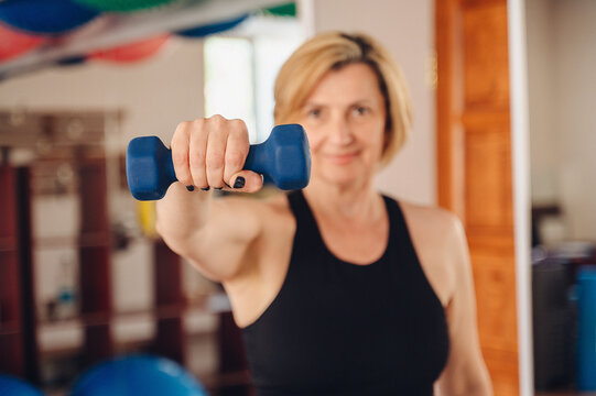 Mature woman lifting dumbbell at the gym, confident gaze