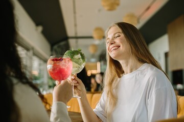 Two young women toasting cocktails in a cafe