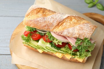 Tasty baguette sandwich with ham, cheese and vegetables on grey wooden table, closeup