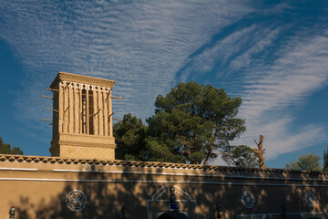 Traditional windcatcher (badgir) rises above an adobe building in Yazd, Iran, under a vivid sky, showcasing Persian desert architecture and natural cooling systems.