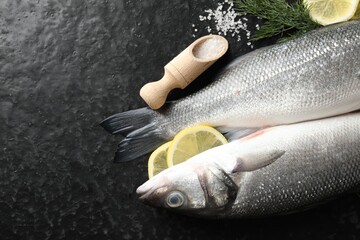 Fresh raw seabass fish with spices on black table, flat lay and space for text. Seafood delicacies