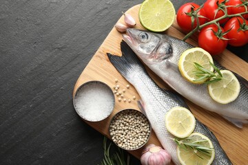 Fresh raw seabass fish with spices on black table, top view and space for text. Seafood delicacies