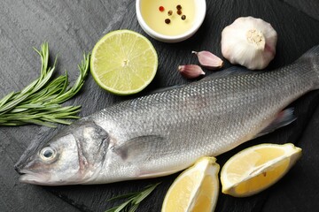 Fresh raw seabass with spices on black table, flat lay. Fish and seafood delicacies