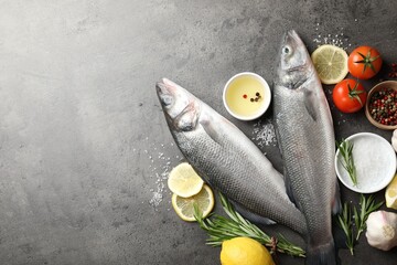 Fresh raw seabass fish with spices on grey table, flat lay and space for text. Seafood delicacies