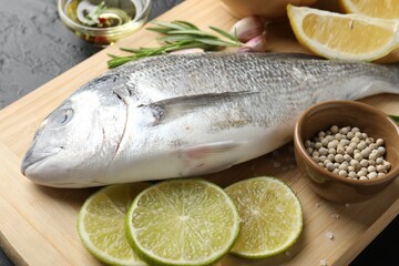 Fresh raw dourade with spices on black table, closeup. Fish and seafood delicacies