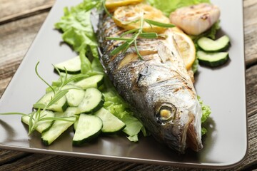 Tasty roasted seabass fish served with vegetables and lemon on wooden table, closeup. Homemade seafood dish