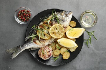Tasty roasted dorado fish served with potatoes, rosemary and lemon on grey table, flat lay....