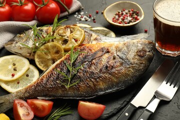 Tasty roasted dorado fish served with beer on black table, closeup. Homemade seafood dish