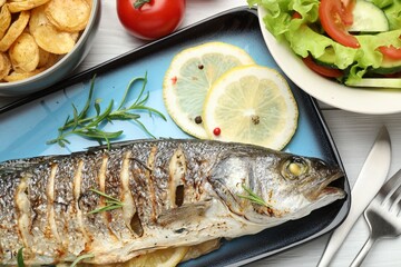 Tasty roasted seabass fish served with salad and potatoes on white wooden table, flat lay. Homemade seafood dish
