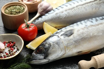 Fresh raw mackerels and spices on black table, closeup. Seafood delicacies