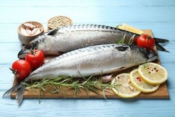 Fresh raw mackerels and spices on light blue wooden table, closeup. Seafood delicacies