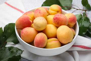Fresh apricots in bowl and green leaves on table, closeup
