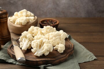 Fresh raw cauliflower florets, spices and knife on wooden table, closeup. Space for text