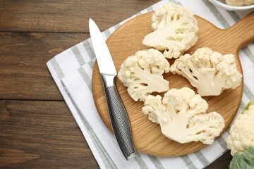 Fresh raw cauliflower florets and knife on wooden table, flat lay. Space for text