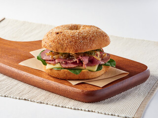 Pastrami and Soft Cheese Bagel Sandwich filled with cream, fresh spinach, and sweet caramelized onions on a wooden board side view of deli menus