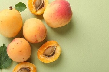 Fresh ripe apricots and leaves on pale green background, flat lay. Space for text