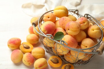 Fresh ripe apricots in metal basket on white wooden table, closeup