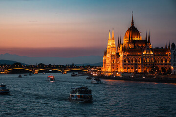 Obraz premium Illuminated Hungarian Parliament Building and boats on the Danube River at dusk in Budapest, Hungary