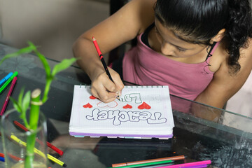 Little Colombian girl carefully coloring in her notebook on a glass table. Painting with her colors