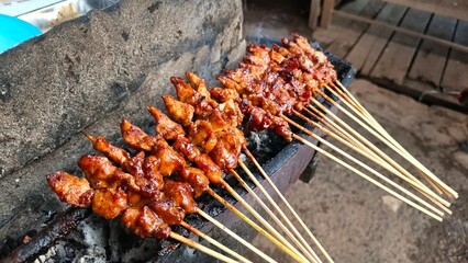 Chicken satay skewers are grilled over a charcoal grill, creating a smoky, flavorful dish. The golden-brown satay is ready to be served and enjoyed.