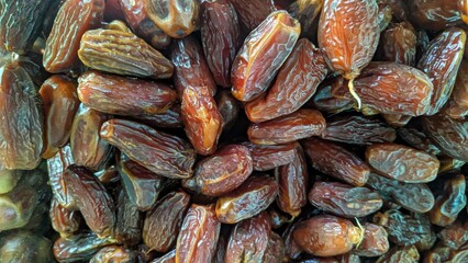 A close-up shows a heap of dark brown dates, filling the frame with their wrinkled textures and oblong shapes, suggesting sweetness and natural goodness.