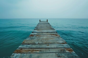 Fototapeta premium Tranquil scene of an aged wooden pier extending into a serene turquoise ocean, evoking a sense of peace and solitude under a soft, overcast sky