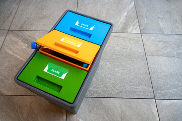Recycling bin with colorful lids for sorting plastic, paper, and organic waste, placed on a tiled...