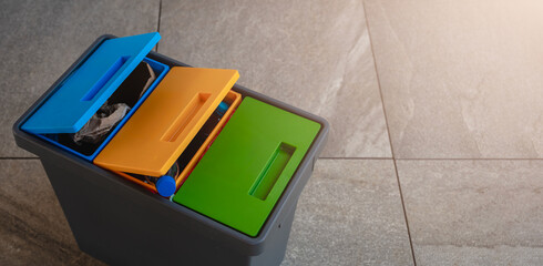 Recycling bin with colorful lids for sorting plastic, paper, and organic waste, placed on a tiled...