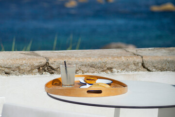 Cascais, Portugal: Outdoor cafe table with a wooden tray, drinks and a traditional Portuguese pastel de nata overlooking a serene harbor filled with sailboats and a clear blue sky