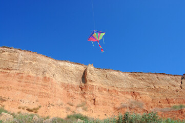 Bright colorful kite flying high above sunlit canyon cliff on a clear summer day. Travel and nature, family vacations, childhood memories, summer leisure, festivals, ecotourism, freedom and lightness