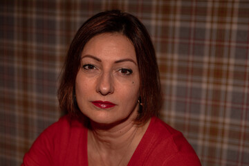 Mature caucasian female in red shirt with short hair against plaid background