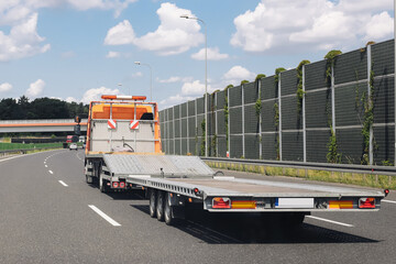 Empty tow truck platform. Orange roadside recovery vehicle driving on highway. Clear blue sky and...