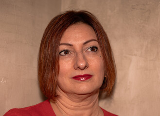 Mature caucasian female with bob haircut and red lipstick in thoughtful pose against textured wall
