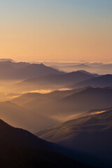 Golden haze drifting across layered mountain ranges at sunrise in tranquil illustration