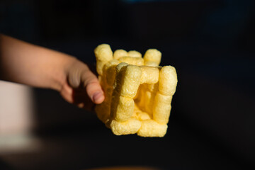 Closeup of child holding a handmade cube built from puffed corn sticks using saliva as adhesive....