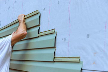Construction worker carefully places installing new pvc vinyl siding siding panels on building...