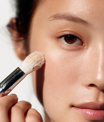 Young beautiful Asian woman applying skin foundation with brush	