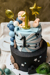 A two-tiered black and blue birthday cake with a baby on top and decorated with baby motifs