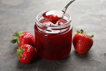 Taking tasty homemade strawberry jam from jar at grey table, closeup
